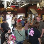 People wait in line and interact at a counter inside a store with various products and displays visible.