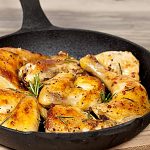 Roasted chicken pieces with herbs in a black cast iron skillet on a wooden surface.