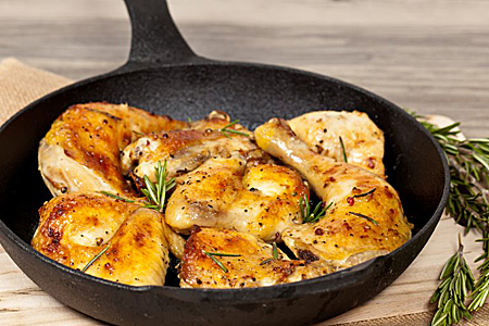 Roasted chicken pieces with herbs in a black cast iron skillet on a wooden surface.