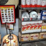Shelves stocked with chick supplies, including feed, waterers, bedding, and a heat lamp with chicks in a bin on the floor.