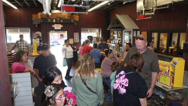 People wait in line and interact at a counter inside a store with various products and displays visible.